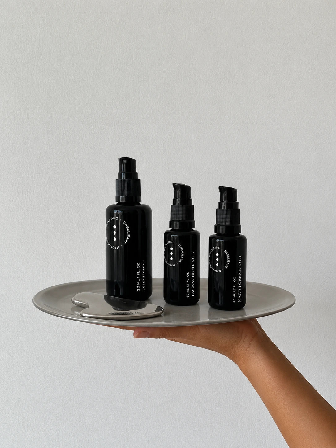 Three Magalie&ME skincare bottles on a tray held in one hand