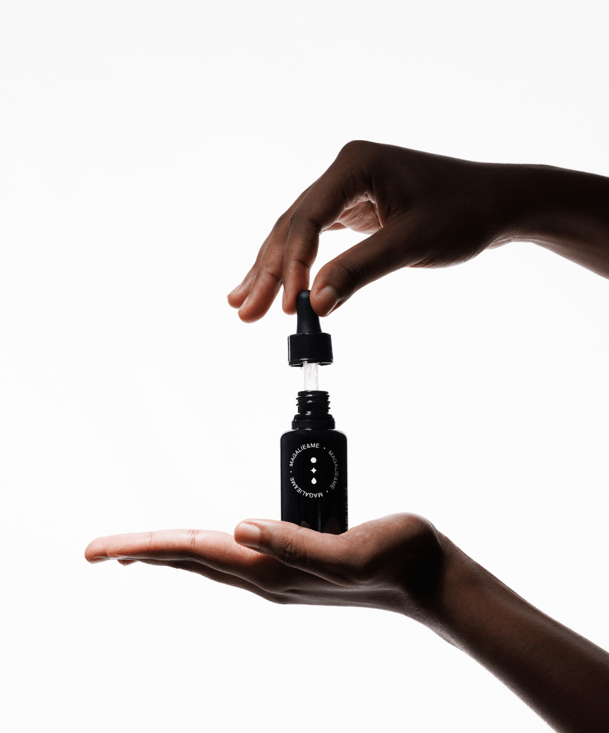 A dropper above a Magalie&ME serum bottle held in an open hand