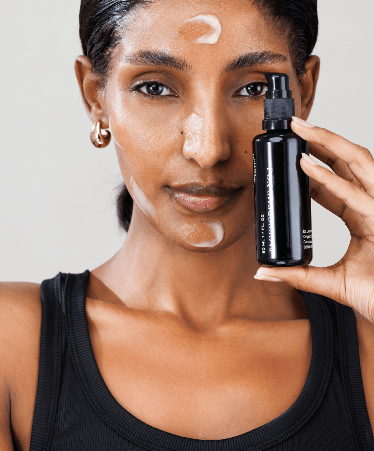 Woman with cream on her face holding a Magalie&ME bottle
